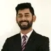 Smiling man with beard and mustache wearing a dark suit and striped tie against a white background.