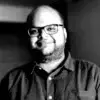 Black and white photo of a smiling man with glasses and a beard wearing a button-up shirt.