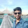 Man wearing sunglasses standing on wooden pier with umbrellas and water in the background.