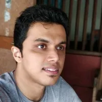 Young man with short curly black hair and gray shirt looking slightly right.