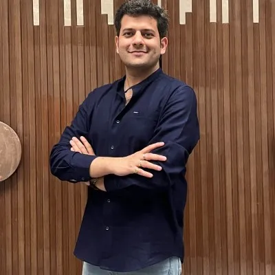 Man in a dark blue shirt standing with arms crossed against a wooden wall with vertical slats.